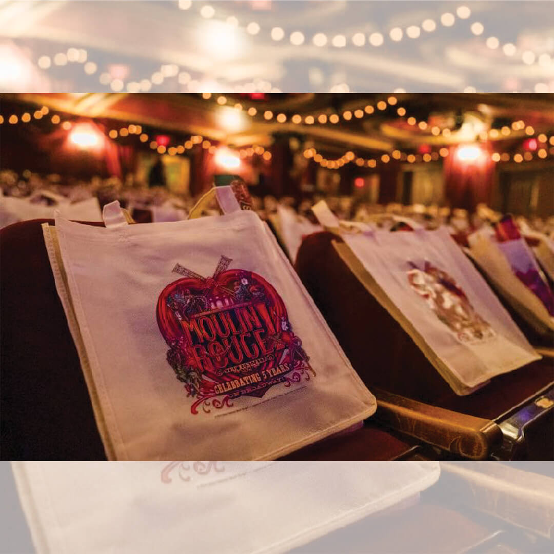 Moulin Rouge branded tote bags placed on theater seats for the audience.
