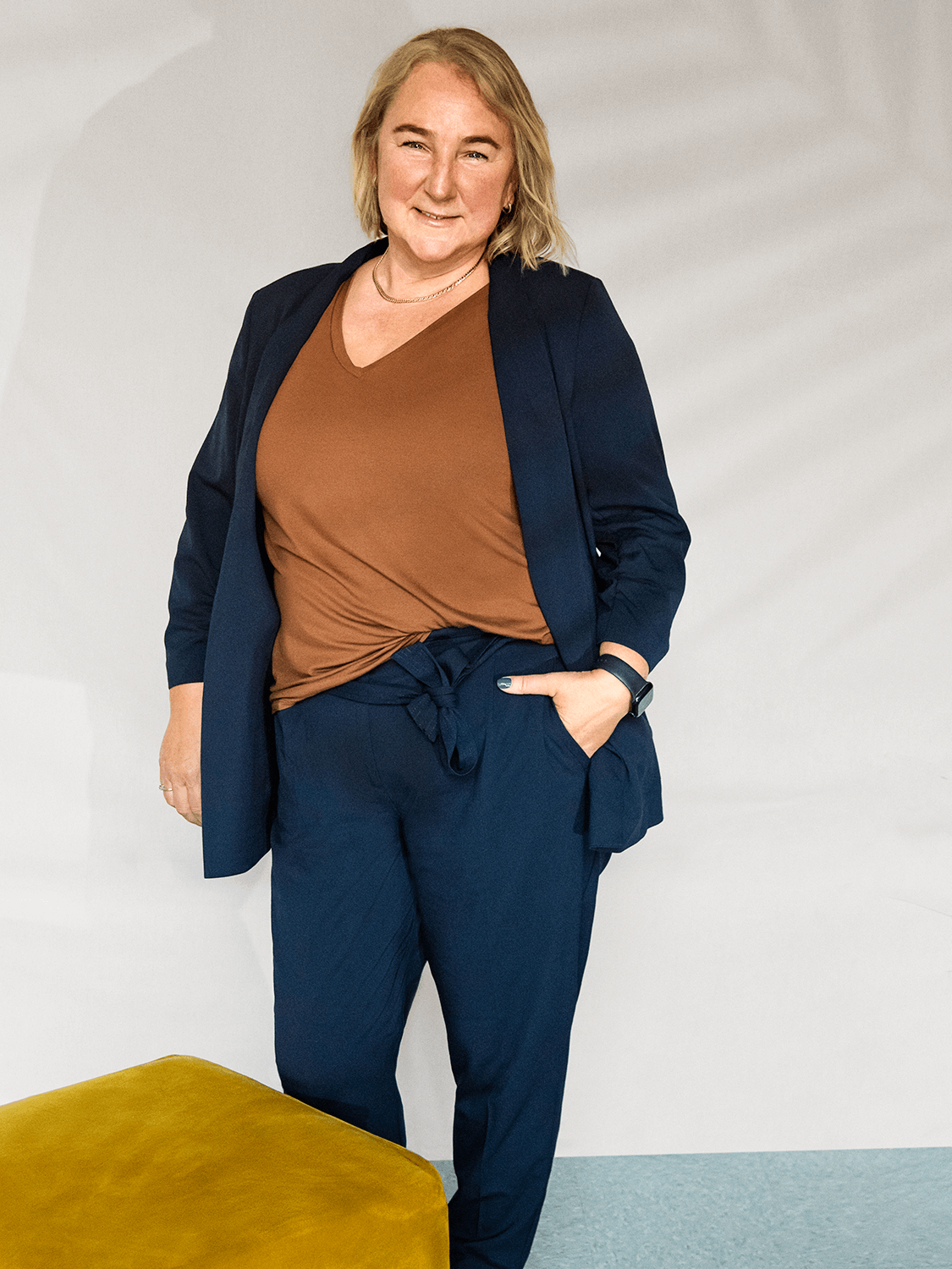 Sue Thoms standing next to a ocher square pouf.